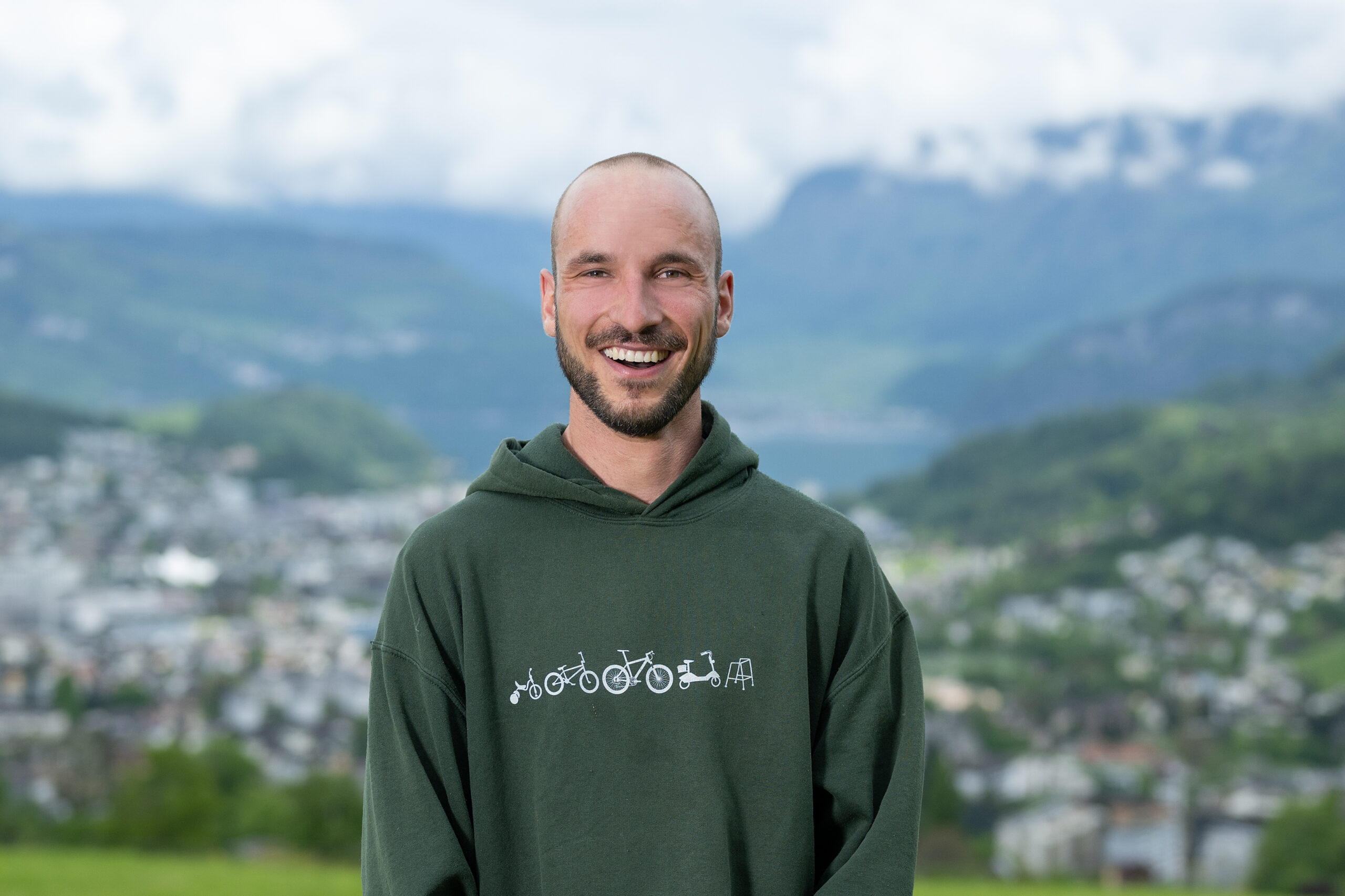 Tandempilot Oli Anken lächelt gut gelaunt im grünen Hoodie vor seinem Lieblingsfluggebiet am Pilatus.