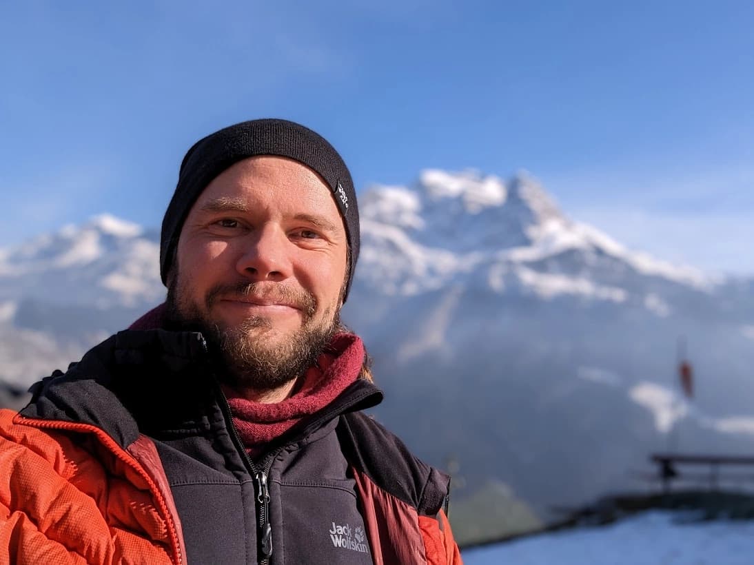 Tandempilot Miki Mohos lächelt in Winterbekleidung vor schneebedeckten Bergen